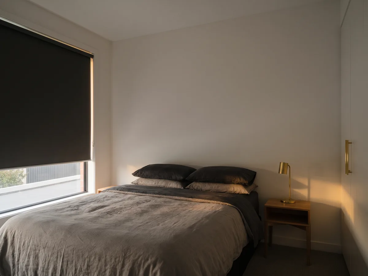 Dark bedroom with blockout roller fully lowered, dawn light held at the window edge